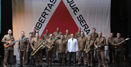 Foto da banda na frente de uma bandeira do estado de Minas Gerais. 